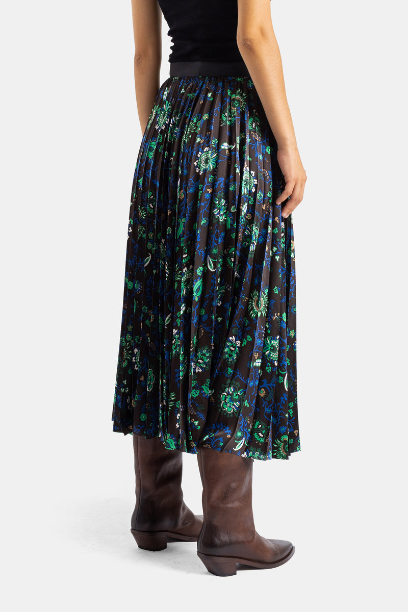 Sacai jupe plissée mi-longue dos, imprimé floral vert bleu sur fond sombre, portée avec bottes cuir marron