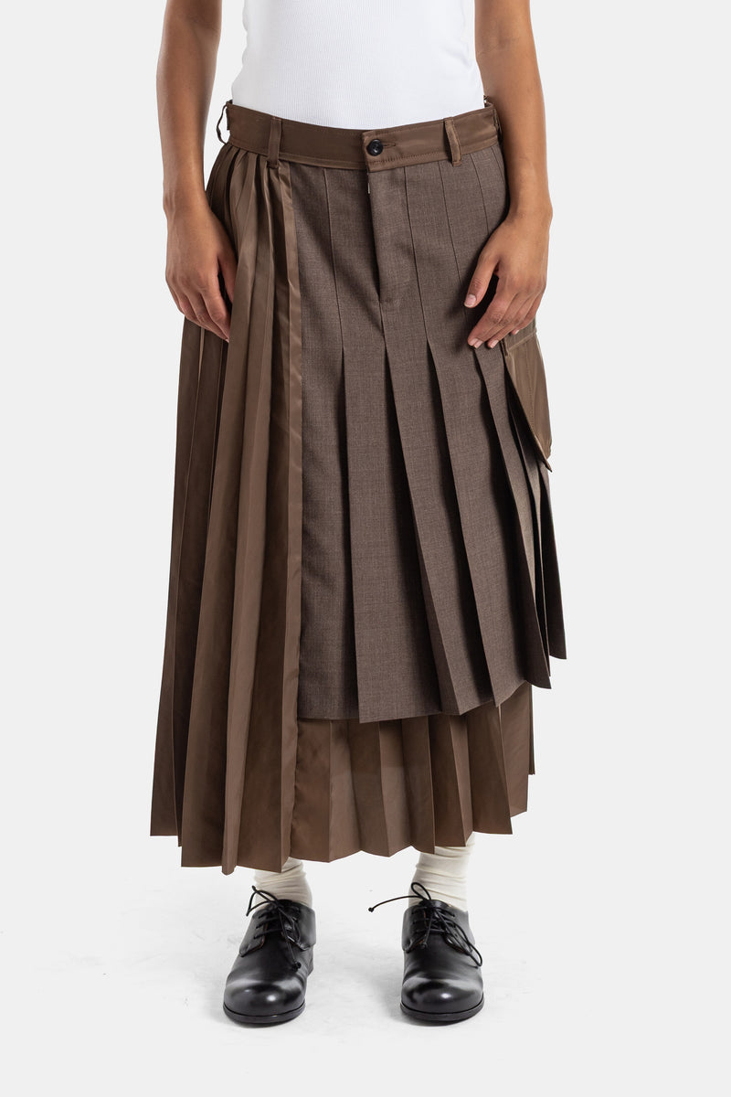 Sacai 타바코 브라운 컬러의 고급스러운 울 소재와 부드러운 새틴이 조화를 이루는 더블 레이어 구조의 플리츠 하이브리드 롱 스커트 제품이며, 풍성하고 여유로운 아방가르드 실루엣이 특징입니다.