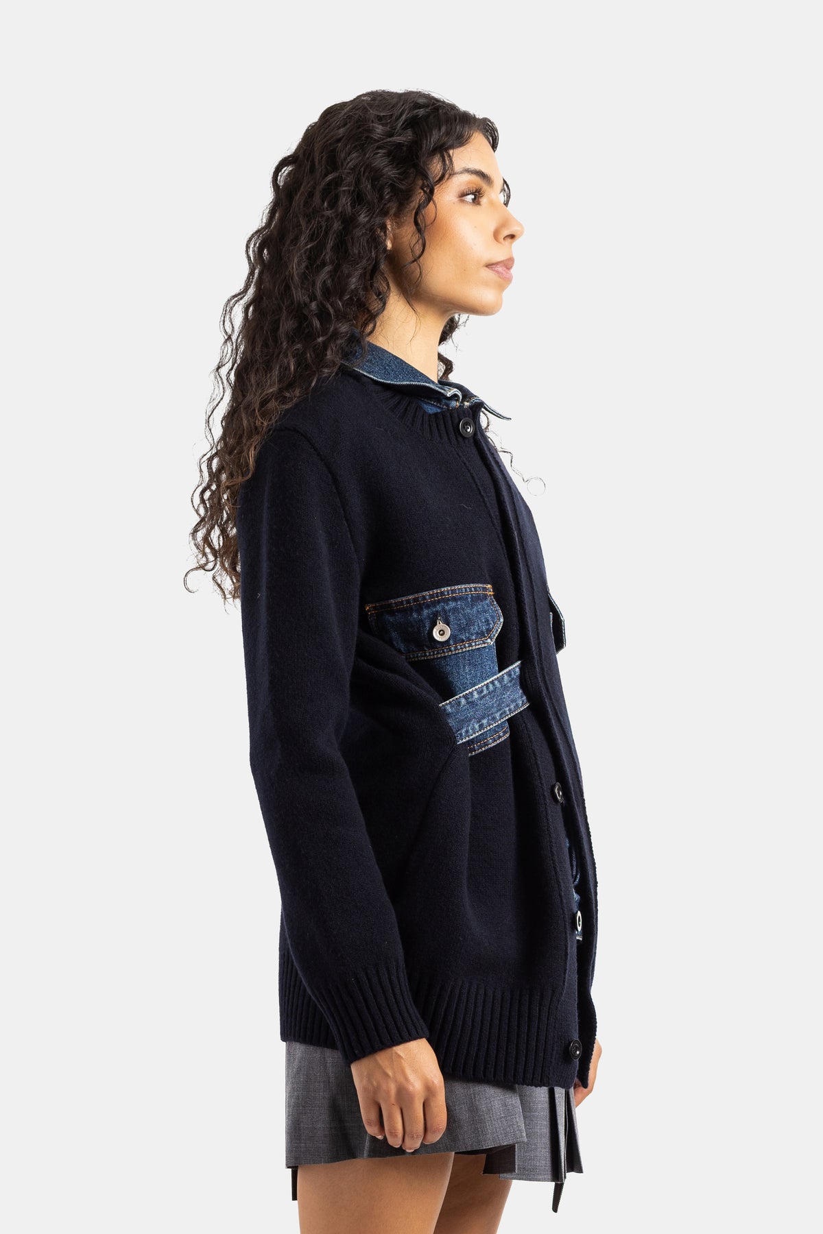 Cardigan da donna Sacai visto di profilo, in maglia di lana blu navy e collo in denim, taglio lungo con bottoni.