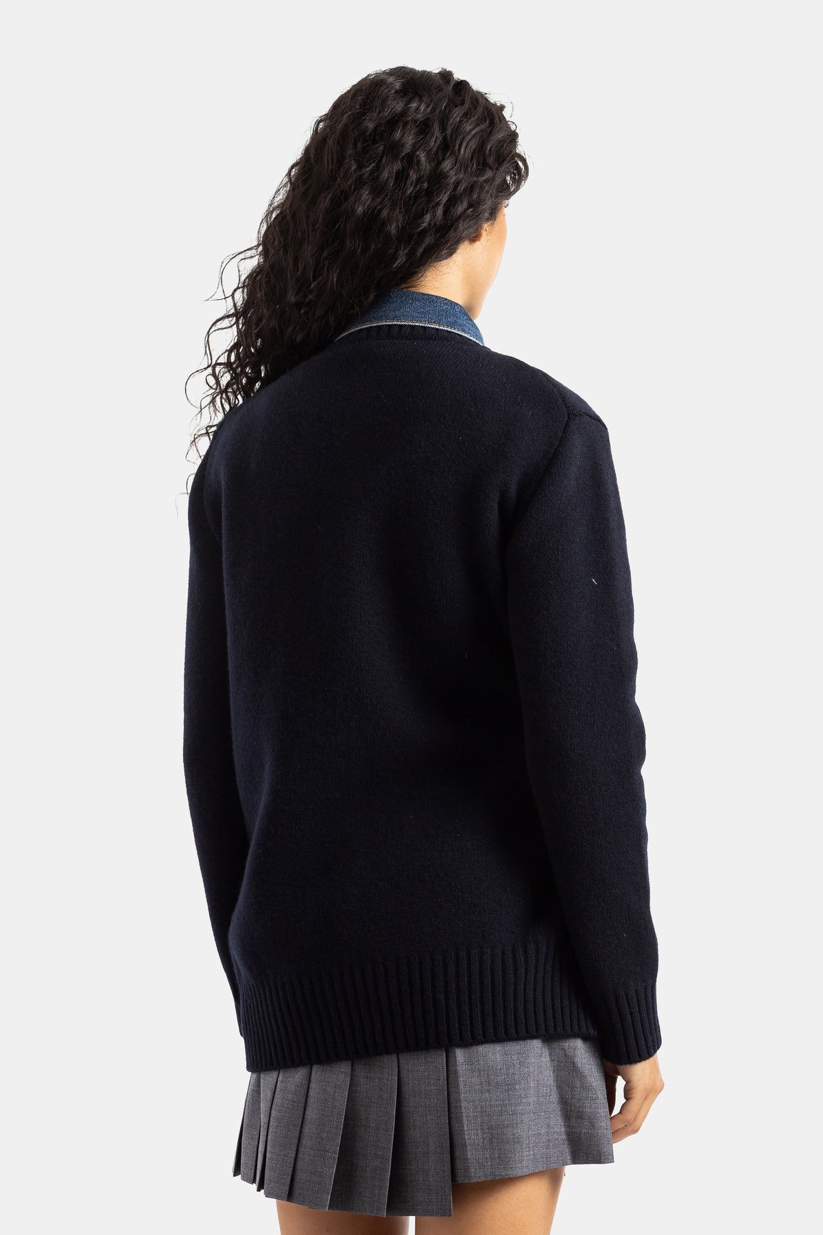 Retro del cardigan Sacai in maglia di lana blu navy con colletto denim a vista, indossato su gonna a pieghe grigia.