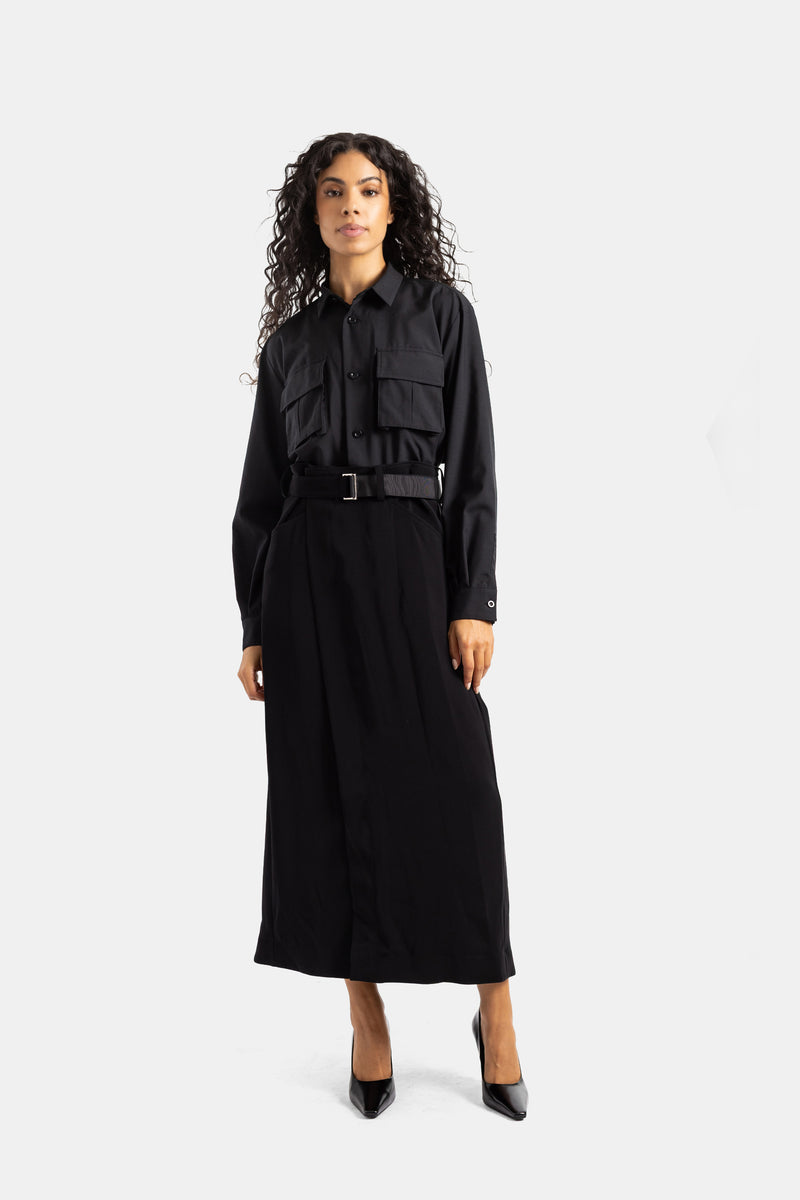 Sacai long black dress with belted waist in front view, showing a fluid silhouette, cargo pockets and satin.