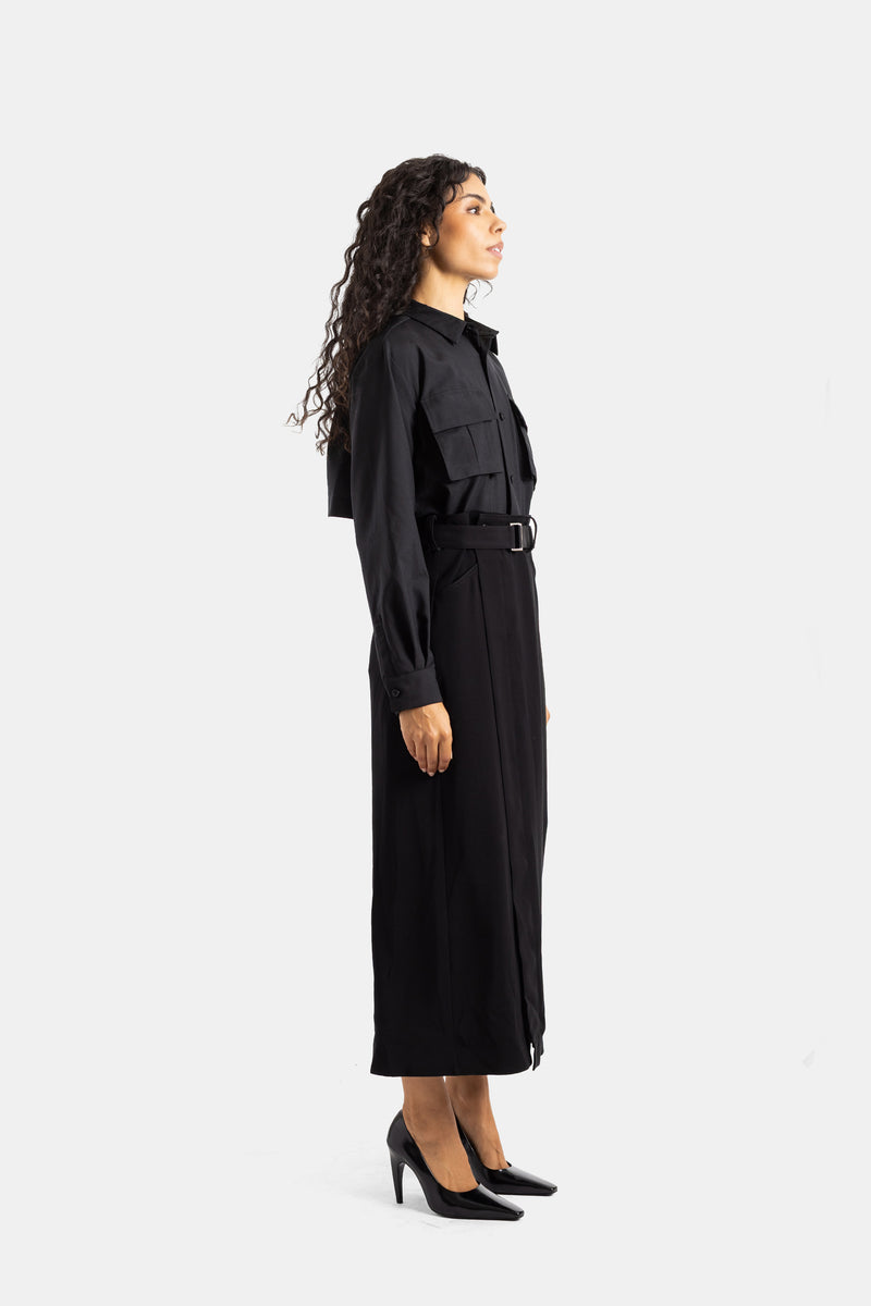 Sacai black midi dress in side profile view, featuring a buckled belt, long sleeves, buttons, and patent heels.