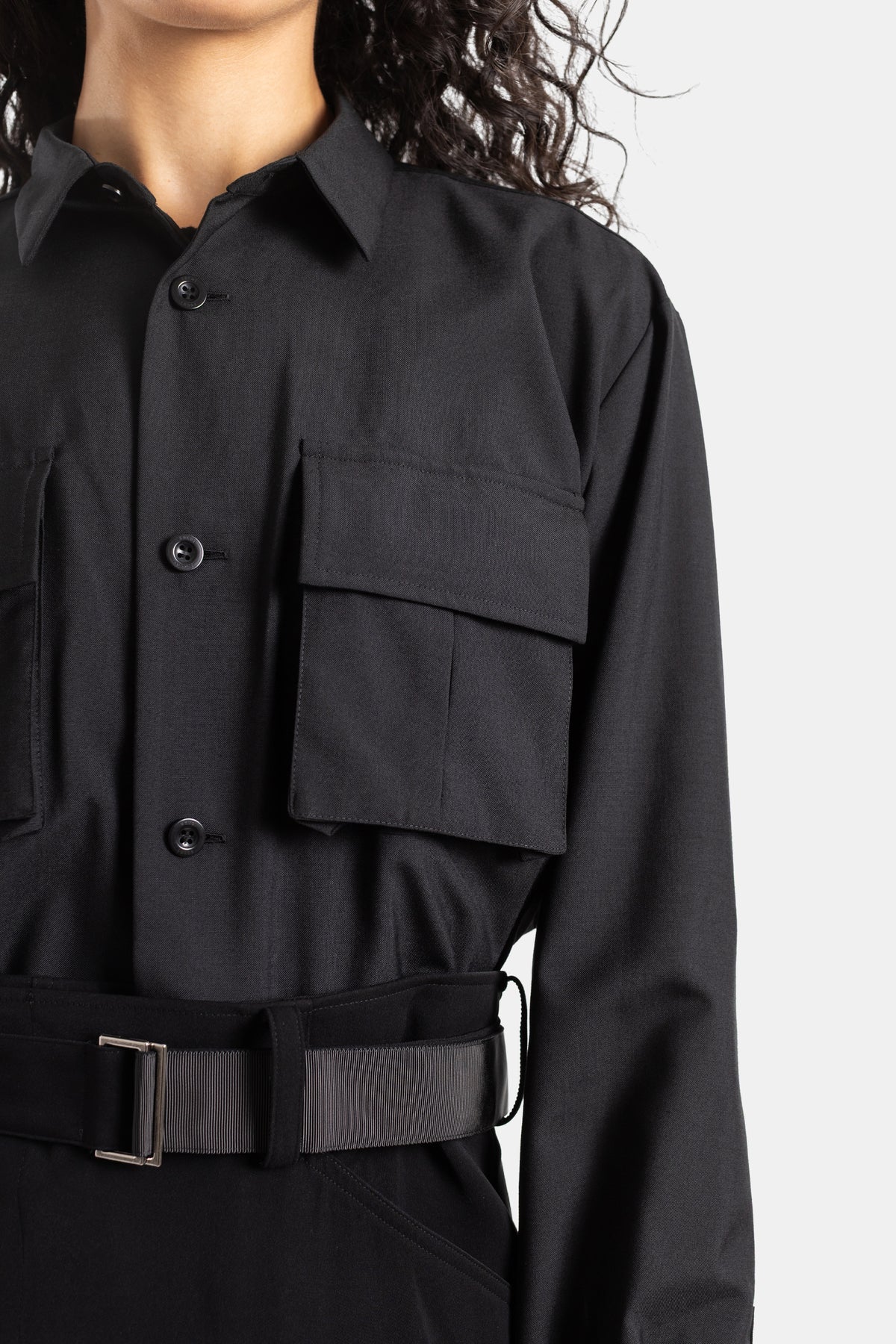 Sacai black dress close-up showcasing cargo pocket, buttons, suiting, large metal buckle belt and texture.
