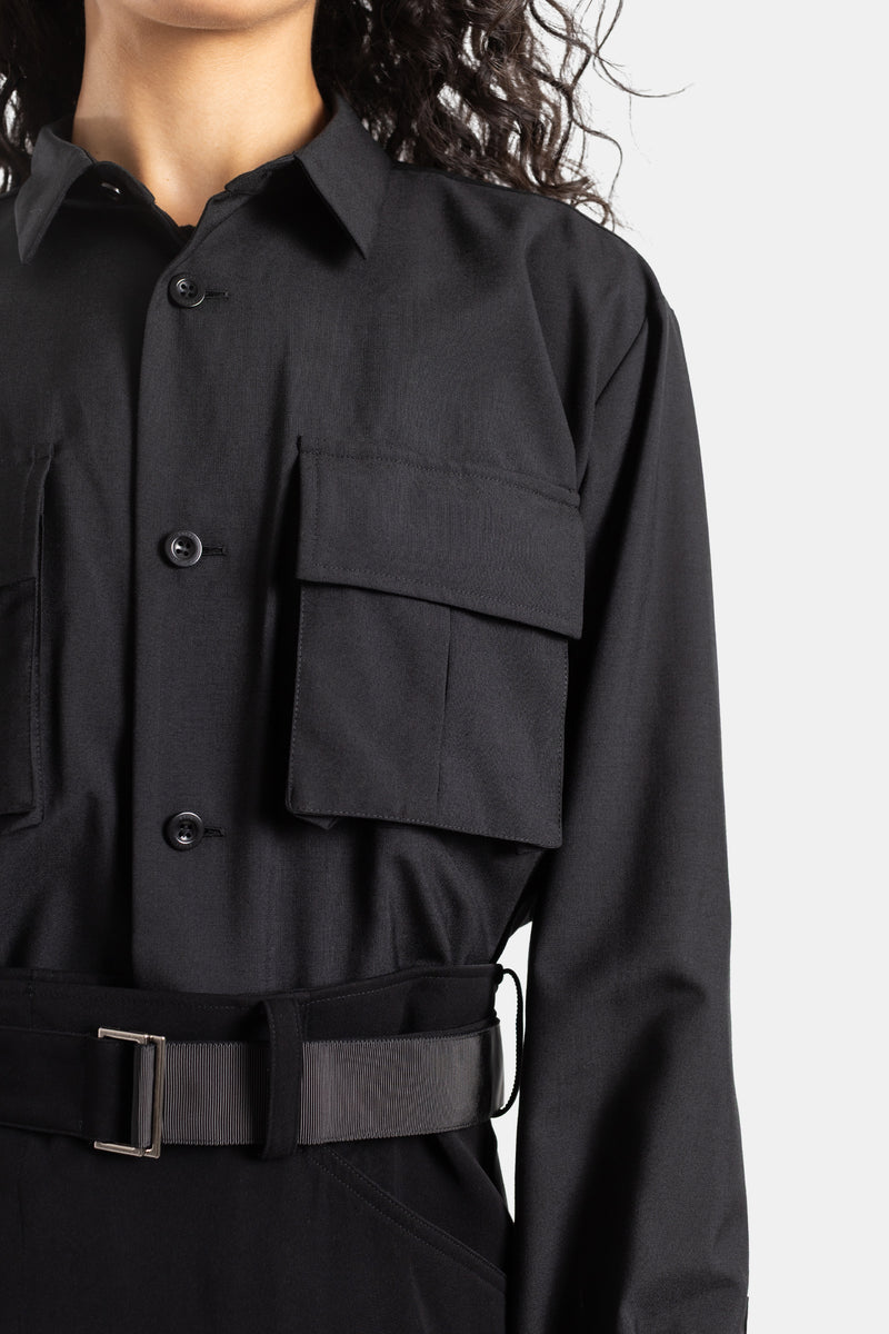 Sacai black dress close-up showcasing cargo pocket, buttons, suiting, large metal buckle belt and texture.