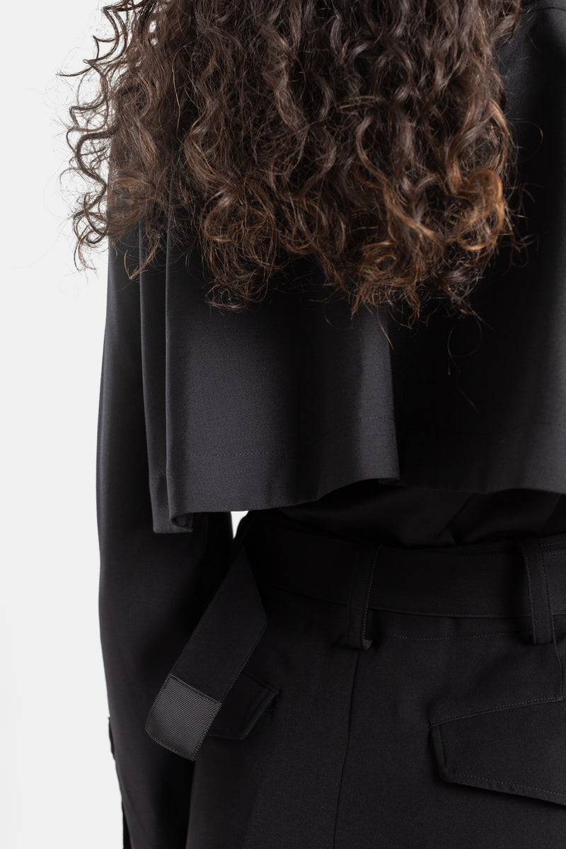 Sacai black dress close-up on layered satin, cape-effect back, curly hair, knotted belt, and fluid fabric.