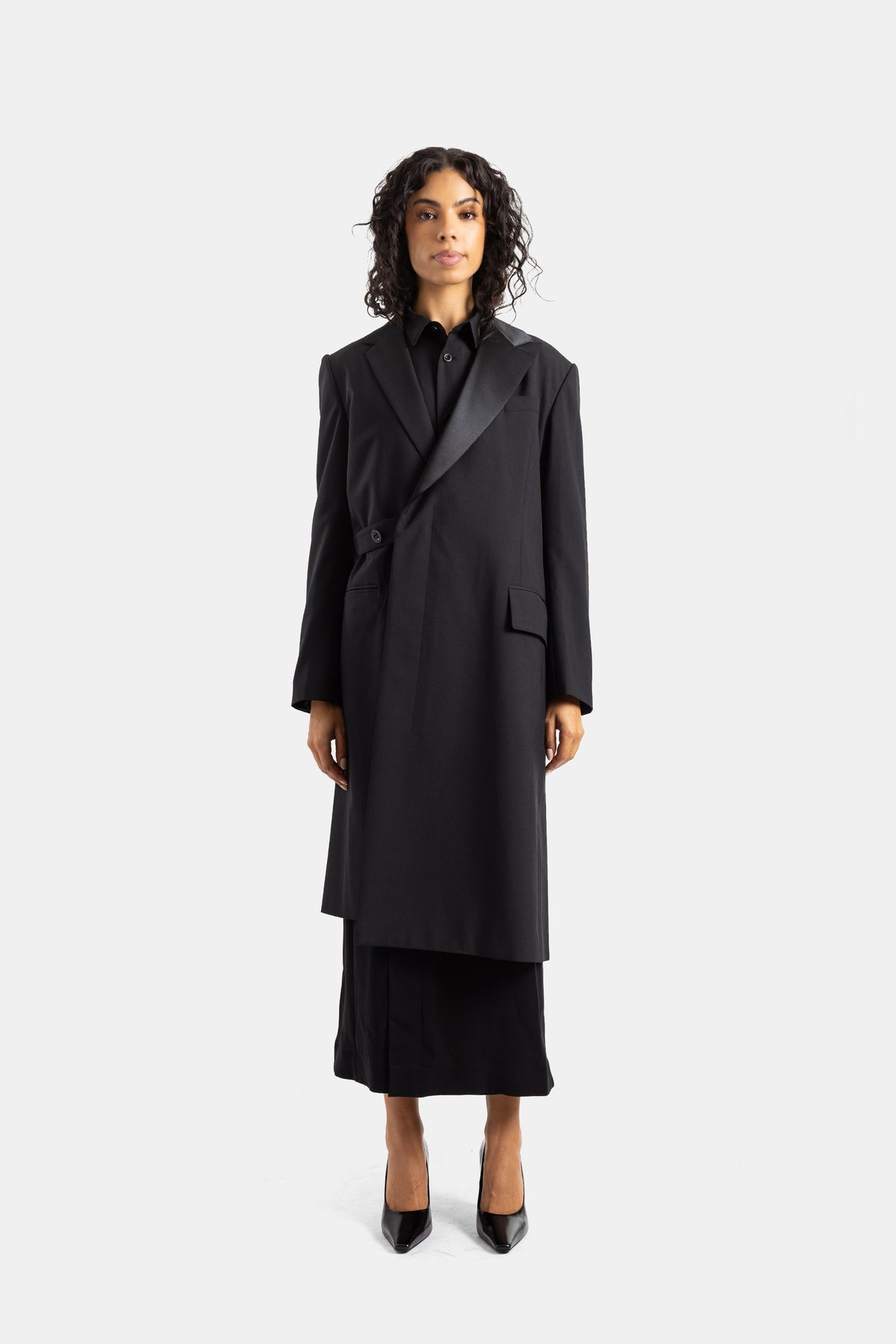 Cappotto lungo asimmetrico nero Sacai in tessuto suiting con revers in raso e taglio oversize strutturato.