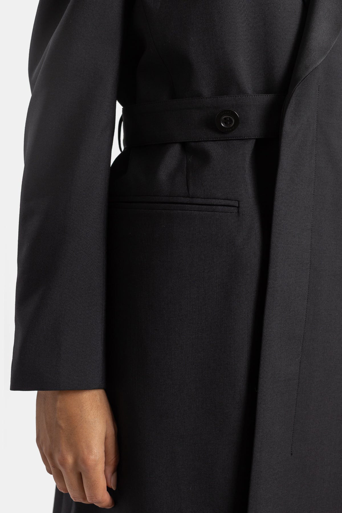 Dettaglio tasca a filetto e cintura abbottonata in vita del cappotto nero Sacai in tessuto suiting elegante.