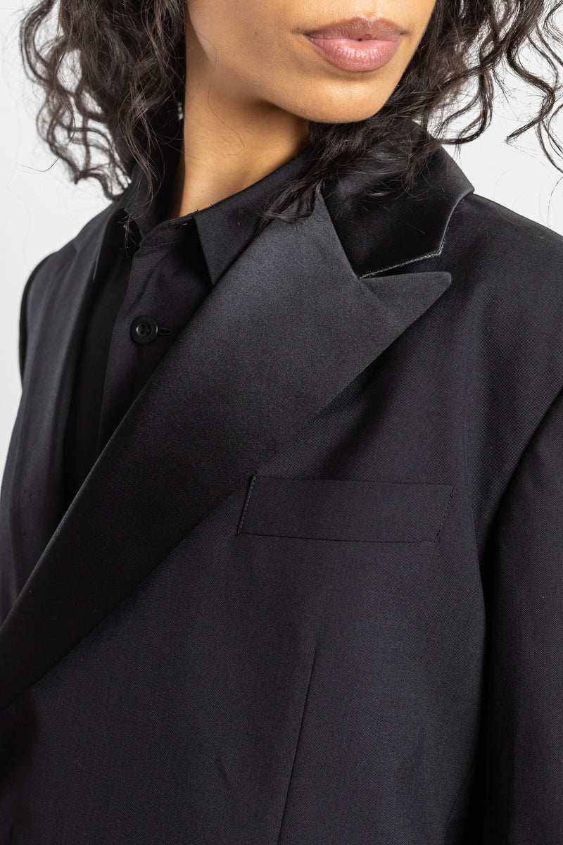 Cappotto nero Sacai con colletto a revers in raso sovrapposto e scollatura asimmetrica incrociata in suiting.