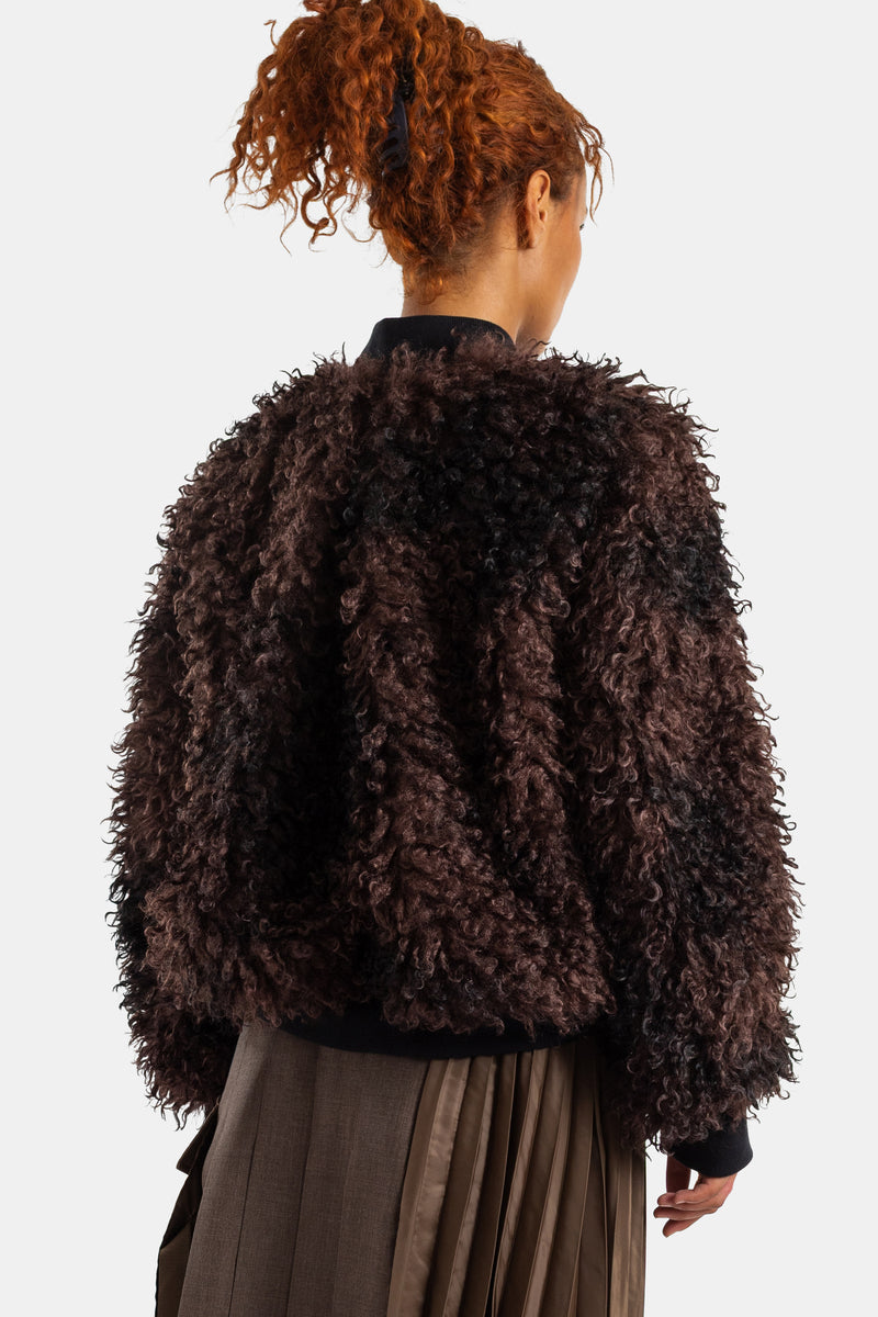 Bomber Sacai em pelo sintético encaracolado castanho visto de costas com detalhe de textura volumosa e punhos pretos.