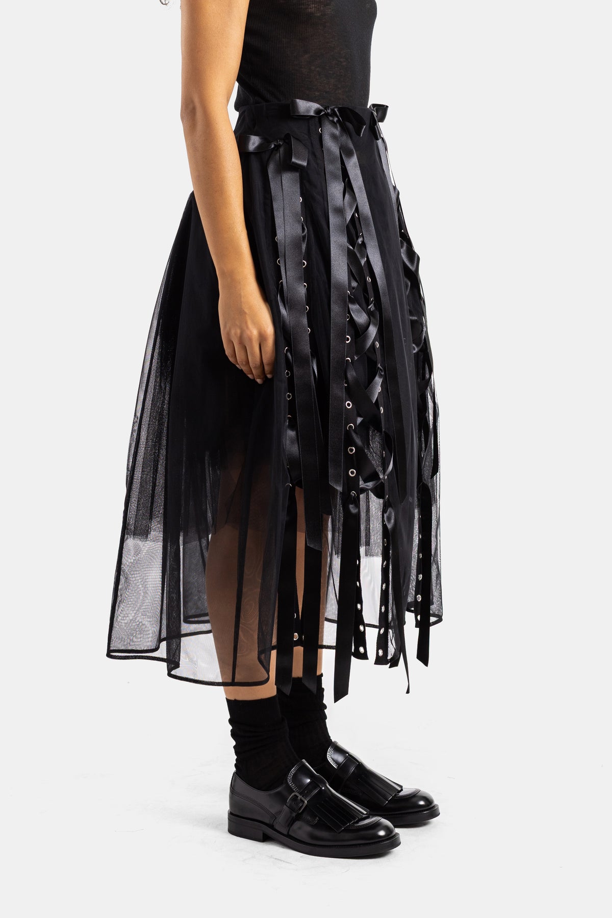 Gonna midi in tulle nero Simone Rocha, vista di profilo con allacciatura in raso e occhielli metallici laterali.