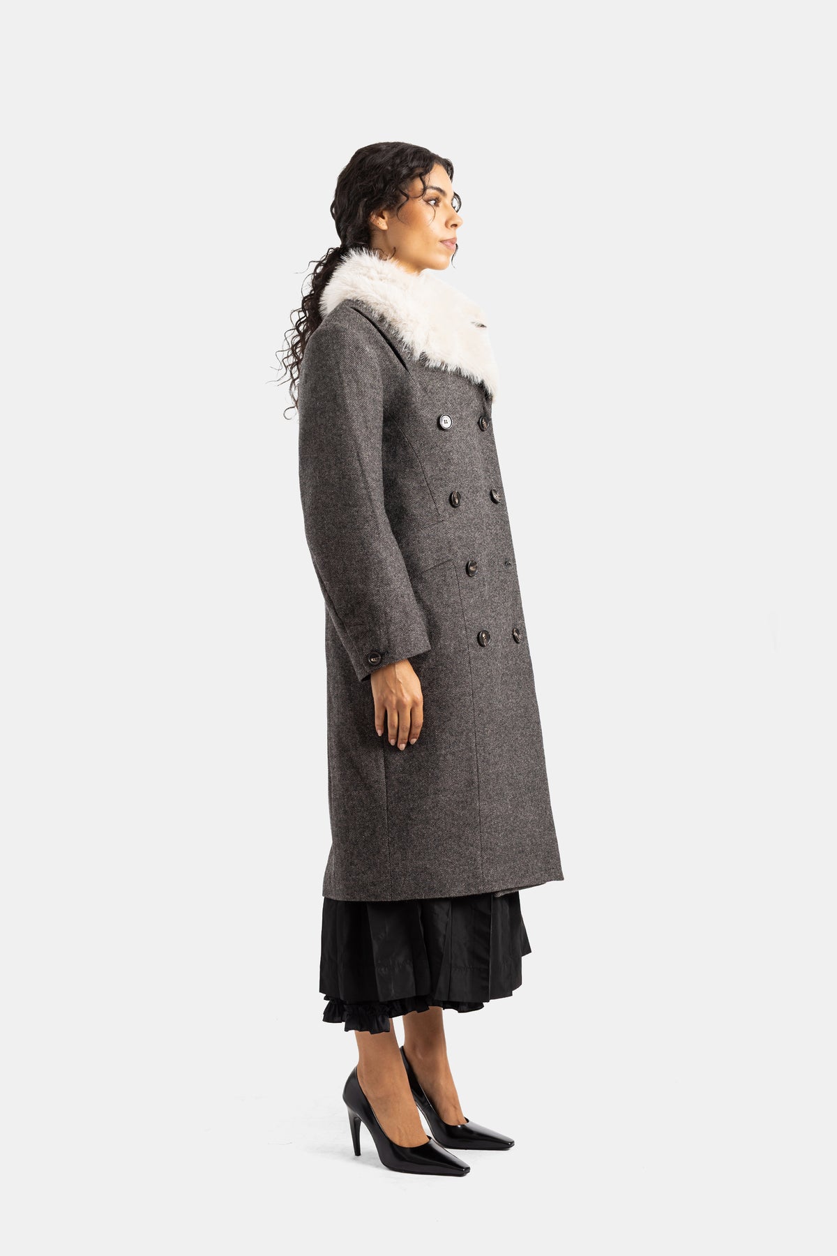Simone Rocha flecked wool coat in profile: long silhouette, white shearling collar, black buttons and stilettos.