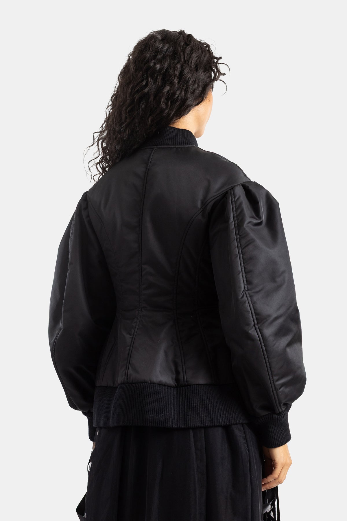 Simone Rocha（シモーネ ロシャ）の黒 of キルティングボンバージャケットのバックスタイル。垂直方向のステッチ、構築的なショルダーライン、そして裾や袖口の厚手のリブニットが特徴の、女性向けモダンアウター。