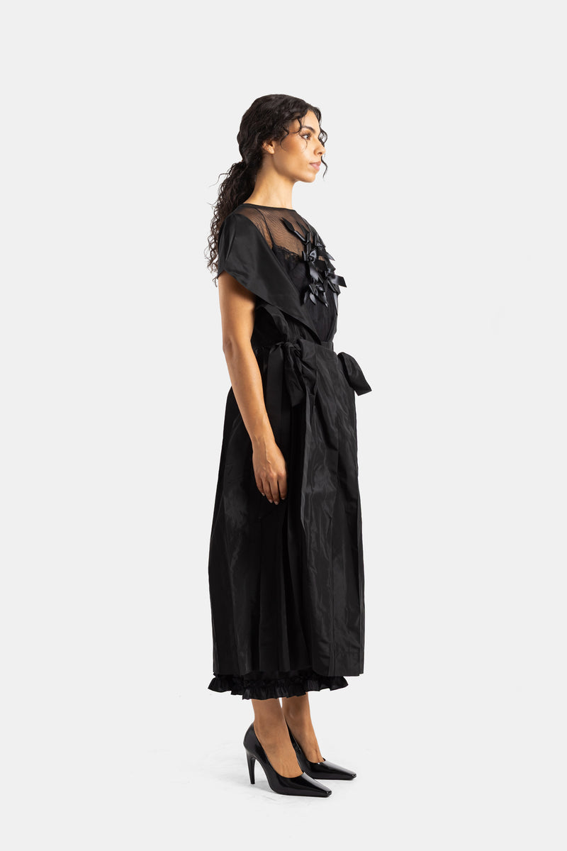 Side profile of the Simone Rocha long black dress featuring a tied waist belt and pleated ruffle hem