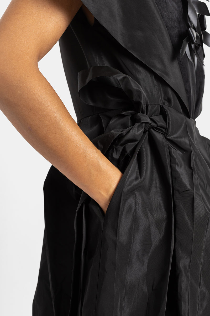 Close-up side view of Simone Rocha black taffeta dress with a tied waist belt and hand in the pocket