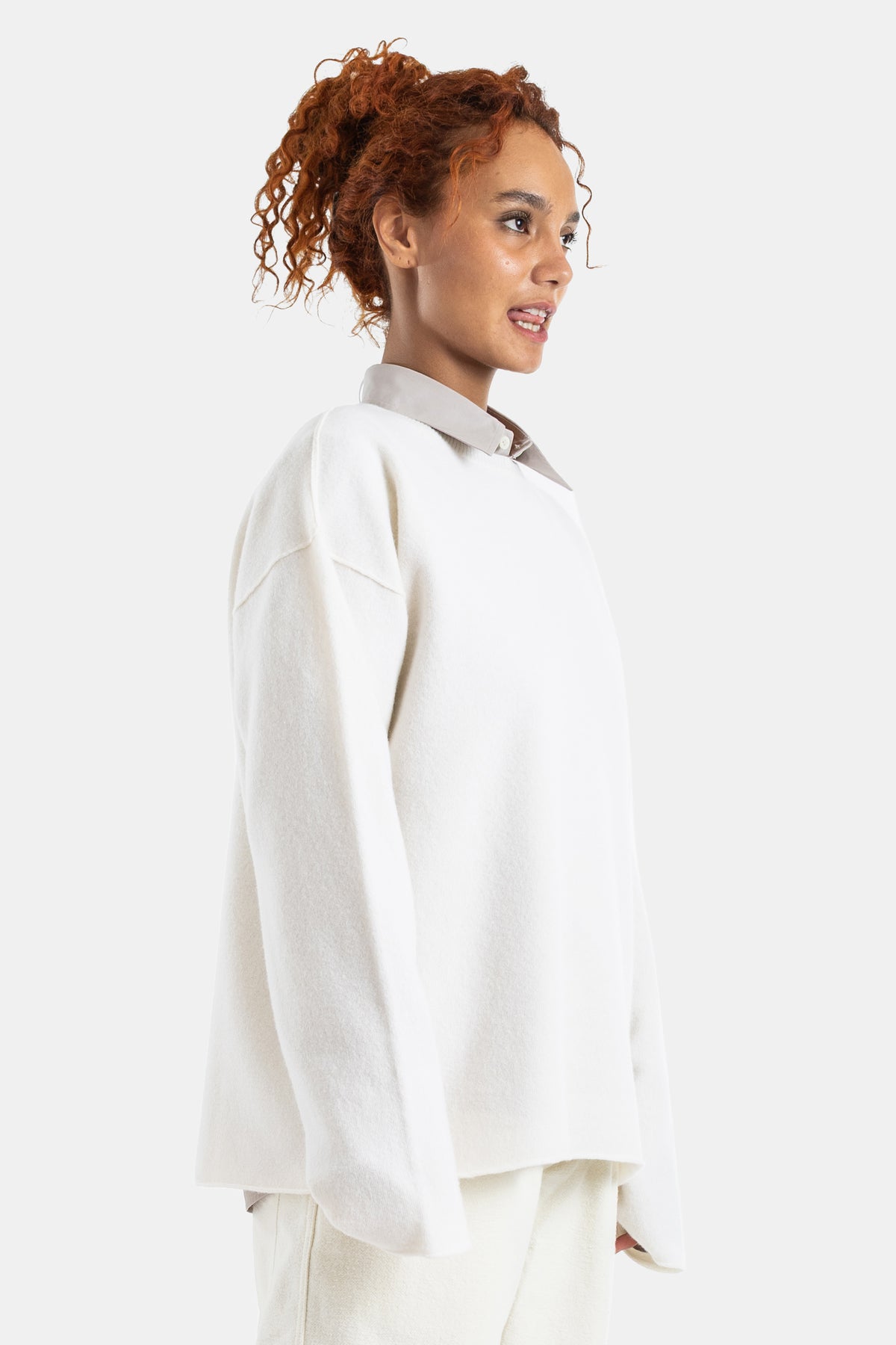 Sofie d'Hoore white wool sweater in a side profile view, oversized silhouette worn over a classic collared shirt