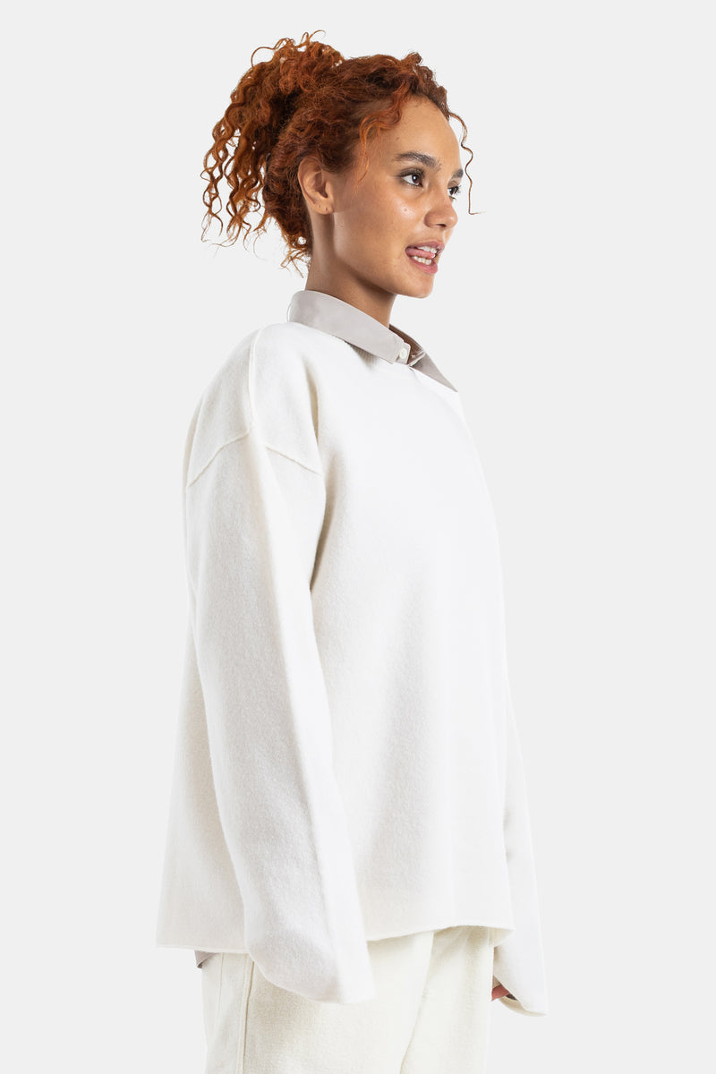 Sofie d'Hoore white wool sweater in a side profile view, oversized silhouette worn over a classic collared shirt