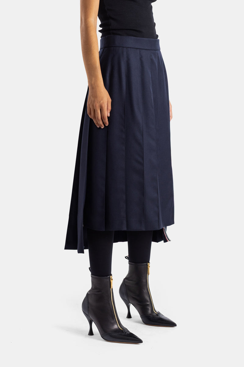 Thom Browne jupe midi plissée marine portée avec legging noir et bottines à talons dorés, vue de côté