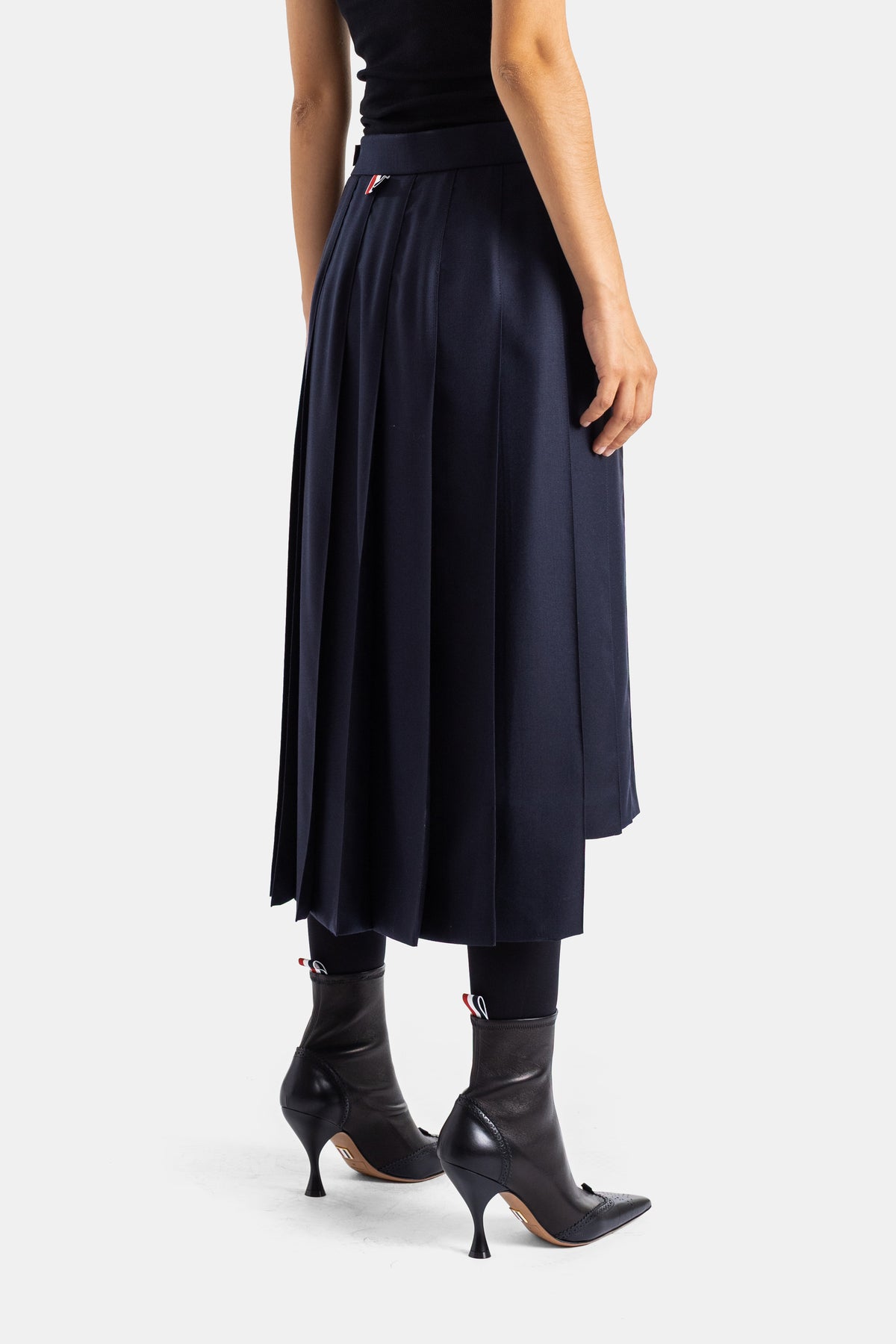 Thom Browne jupe plissée midi marine vue dos, détail plis éventail et étiquette tricolore, portée avec legging et bottines cuir