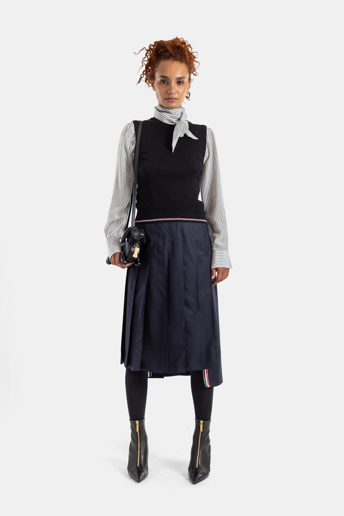 Thom Browne gilet côtelé noir porté sur chemise rayée avec jupe plissée marine, look femme complet