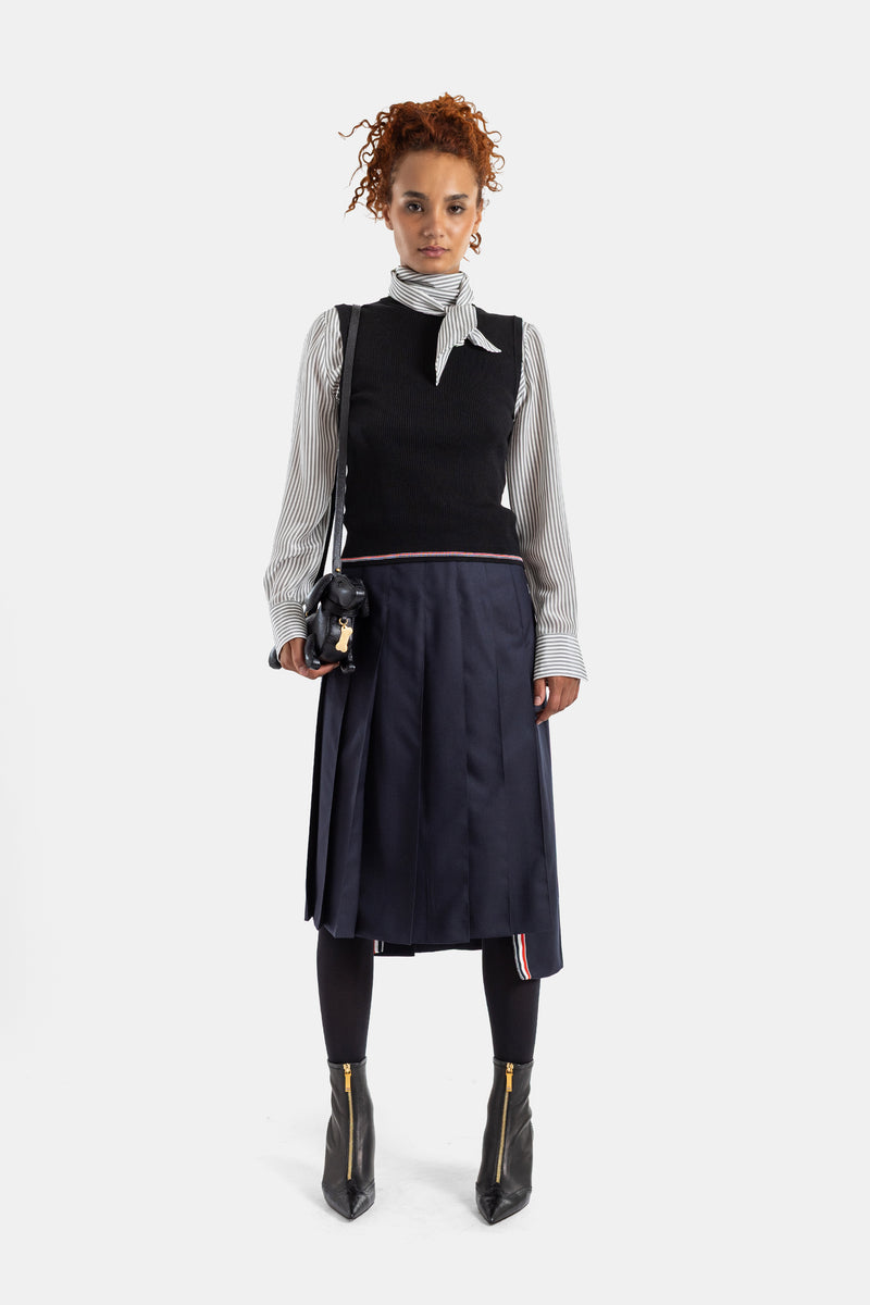 Thom Browne gilet côtelé noir porté sur chemise rayée avec jupe plissée marine, look femme complet