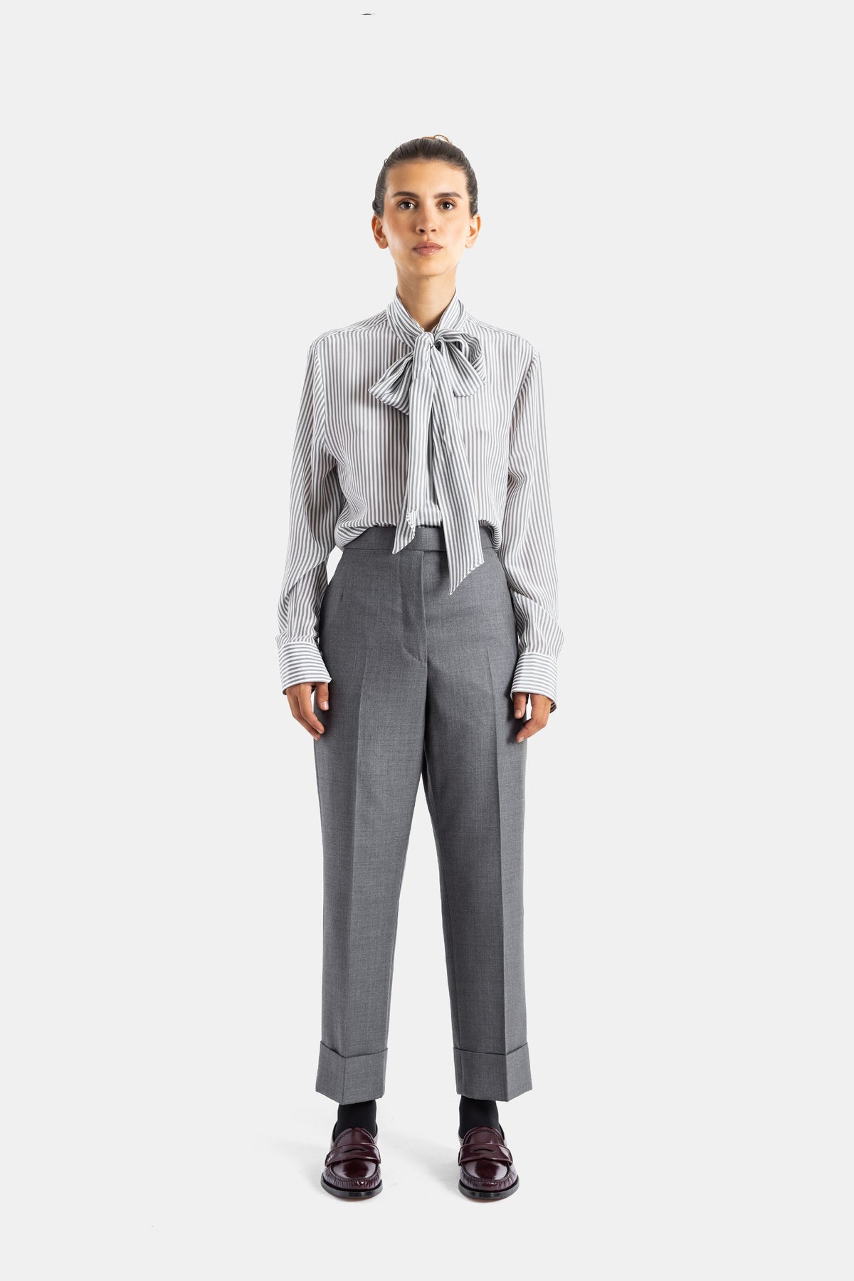 Thom Browne chemise soie rayée lavallière nouée portée avec pantalon tailleur gris et mocassins bordeaux femme