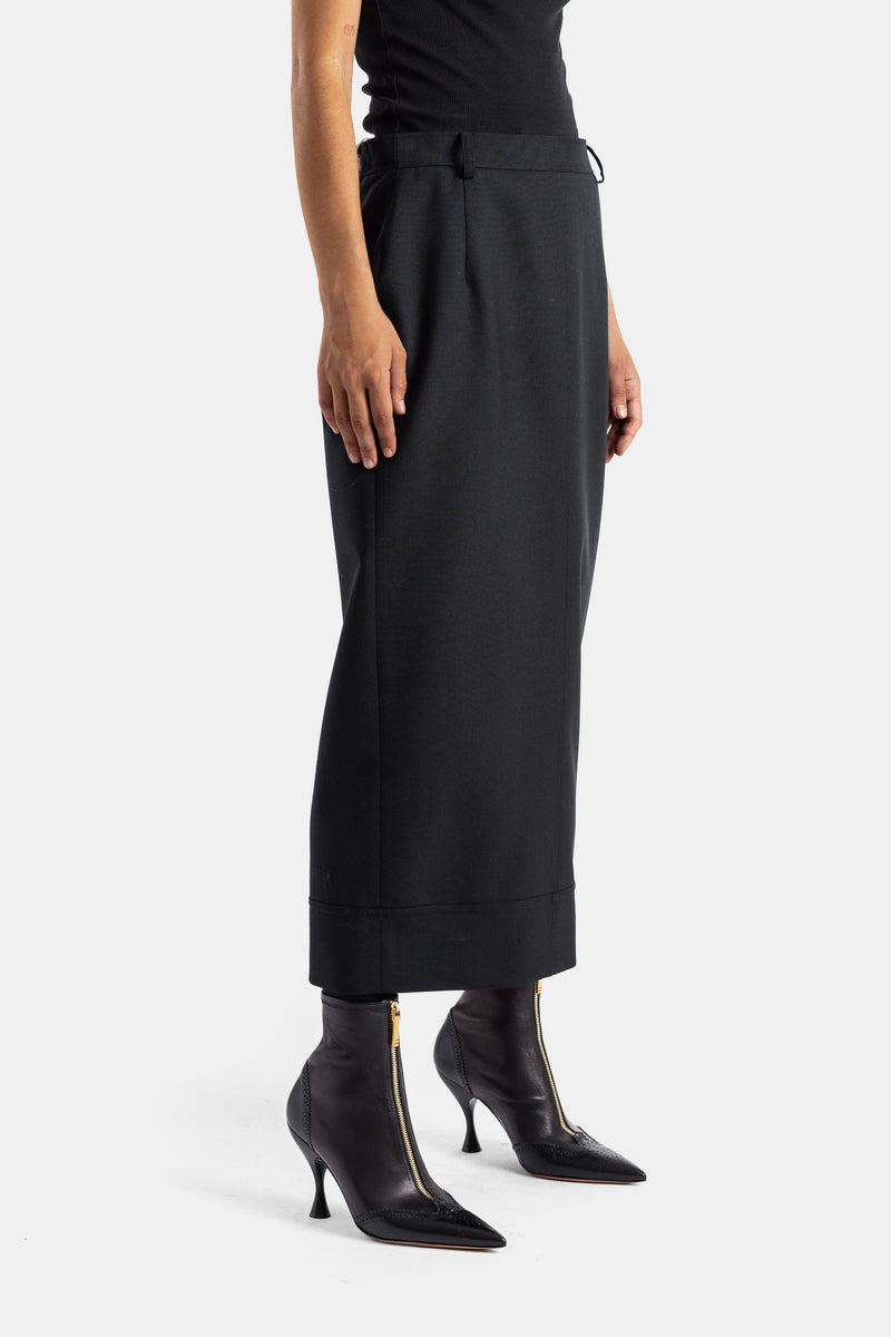 Thom Browne jupe mi-mollet noire portée avec bottines à talon pointu et zip doré, vue de profil